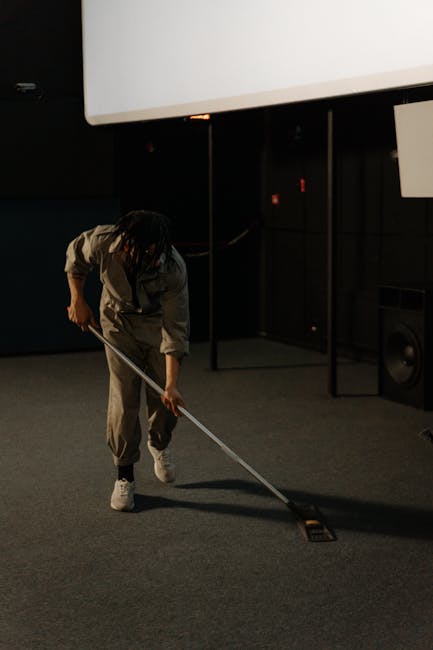 A professional cleaner from Hackney Wick Carpet Cleaners dressed in white protective clothing, including a hood, gloves, and blue shoe covers, using a wet vacuum or steam cleaning machine to deep clea